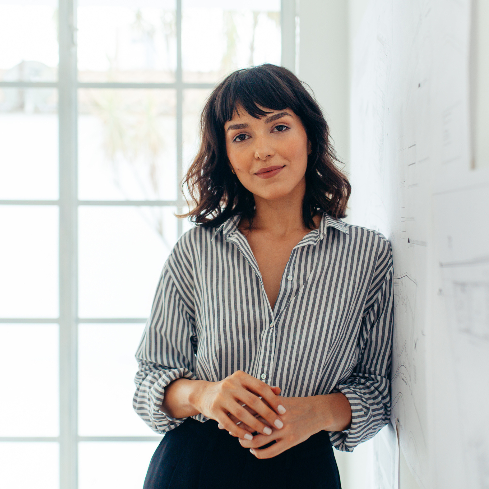 Woman in a striped shirt standing beside a whiteboard in a bright office.